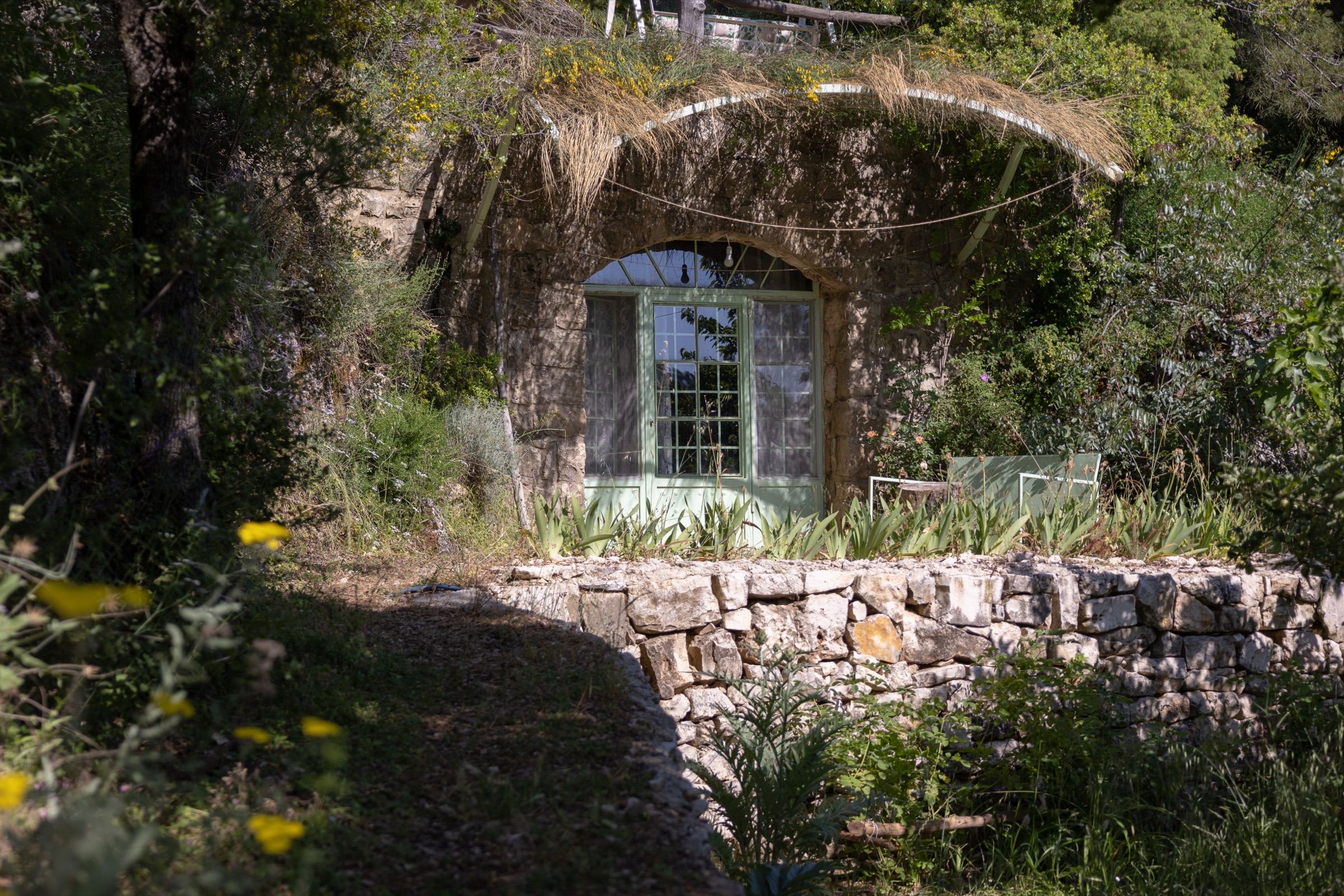 A vine-covered stone building at the end of a dry-stone garden path, its arched window catching the light