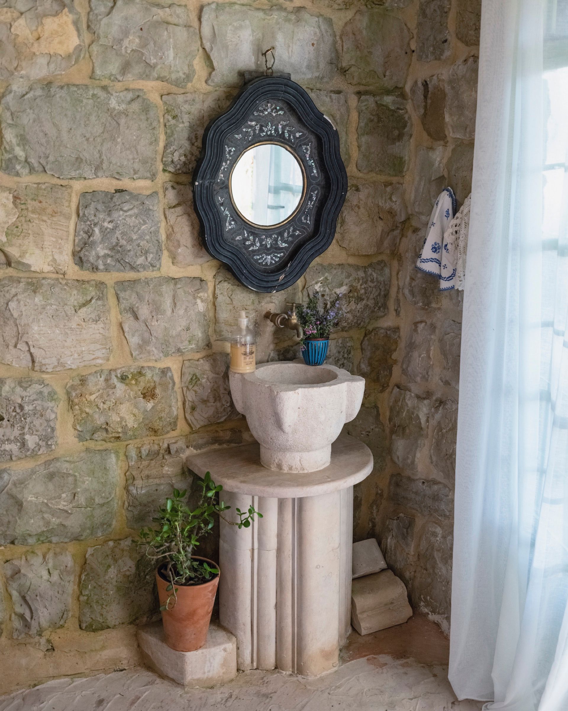 A carved stone basin set against the bare stone wall of the Ermite room, beneath a dark round mirror