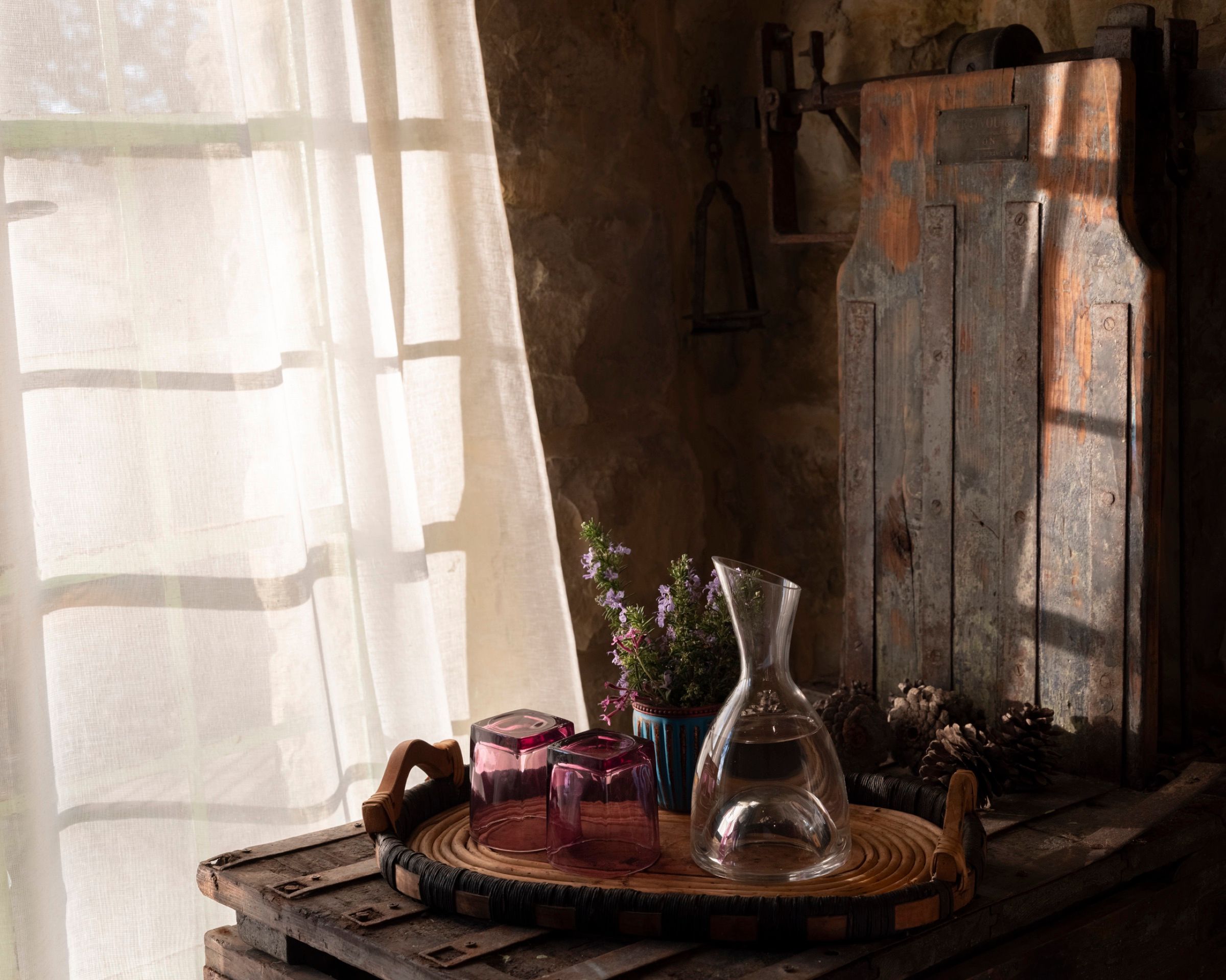 Morning light through a linen curtain in the Ermite room, falling on a glass carafe and a wooden table