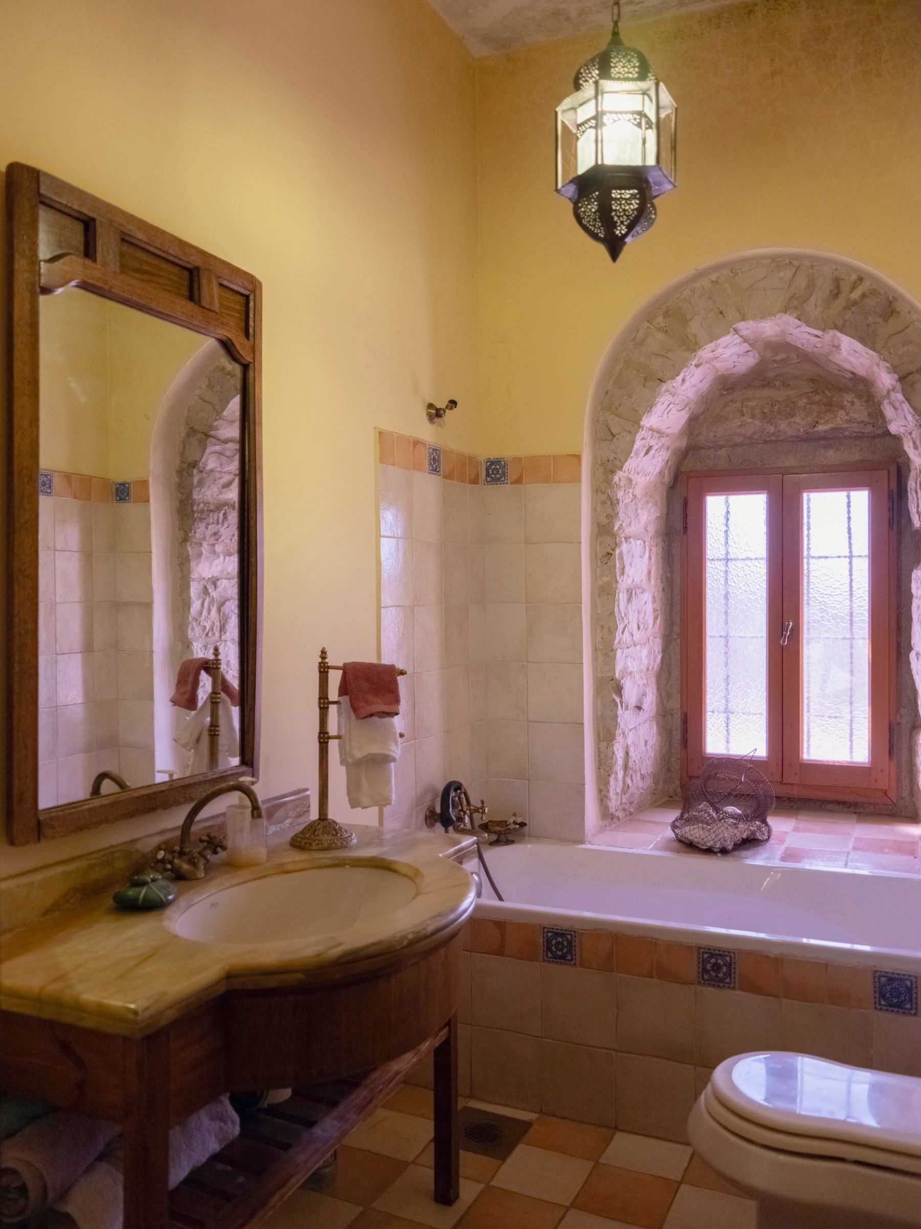 A bathroom in the old monastery, with an arched stone window recess, ochre walls and a stone bath surround