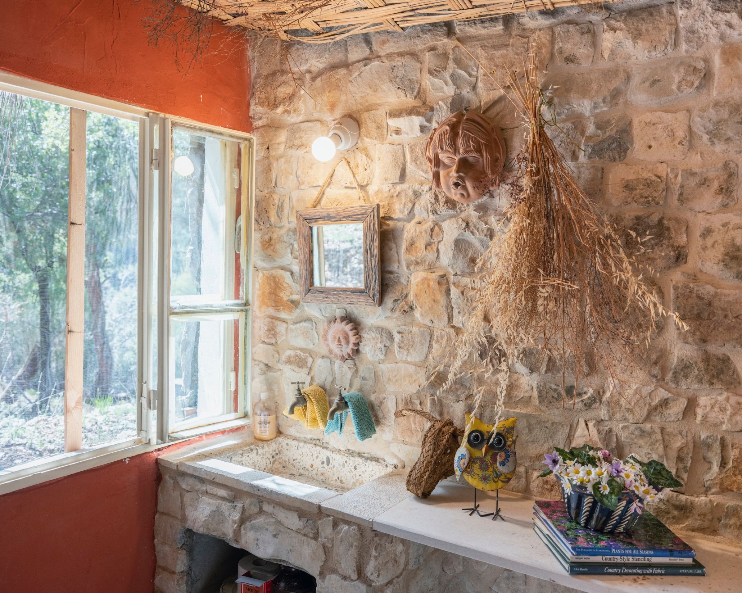 A stone basin set into the wall of the Rosemary room beneath a small wooden mirror, with dried grasses hanging alongside