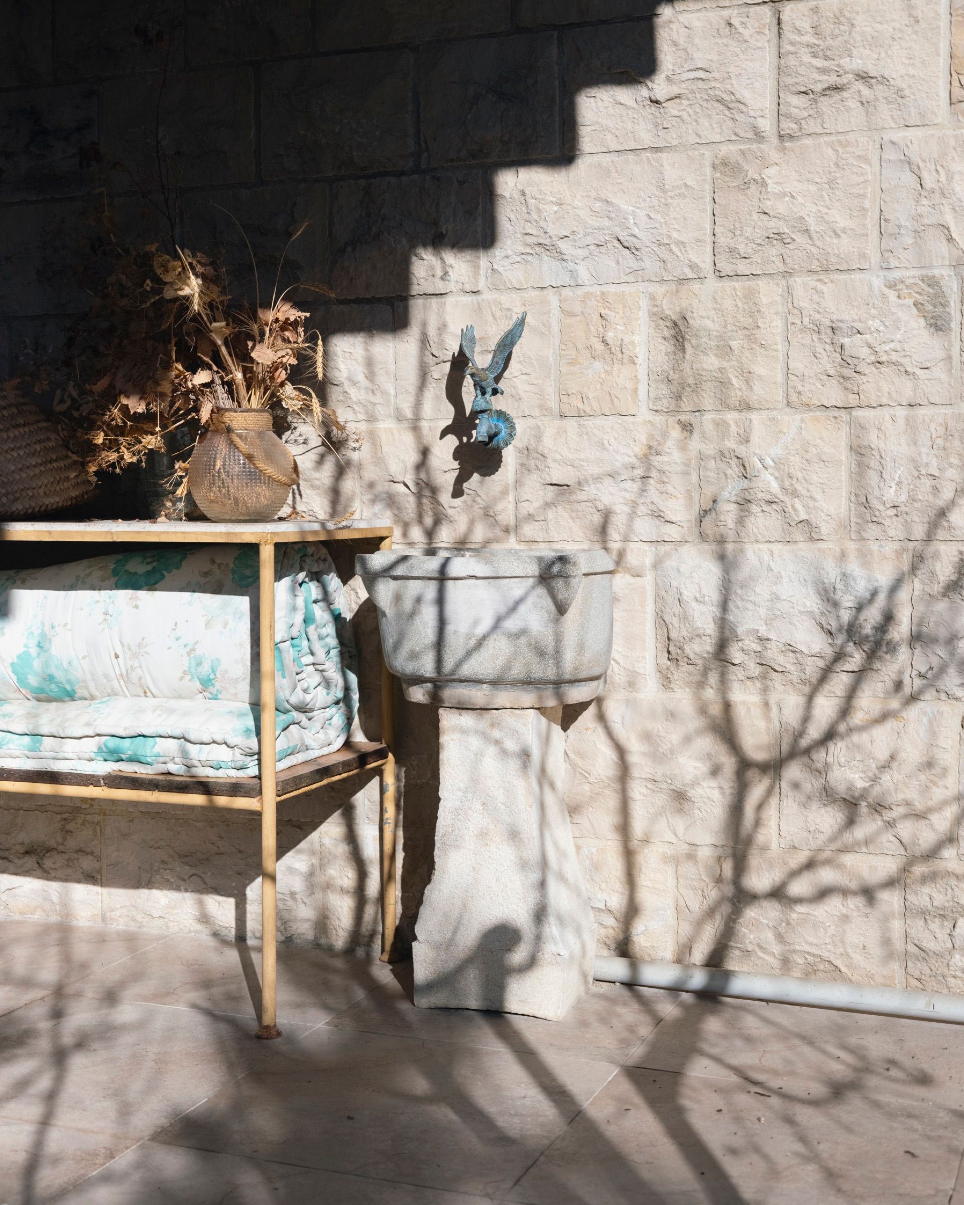 Bare tree shadows falling across a limestone wall beside a stone stair, with a glass-topped table below