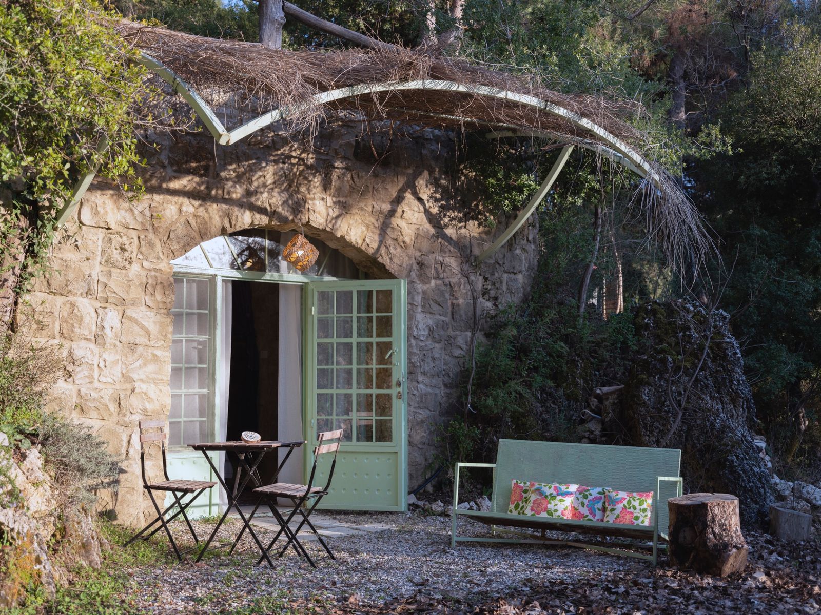 The old stone façade of the guesthouse with a bare vine trained across it, a pair of French doors, and a bench set outside in the morning sun