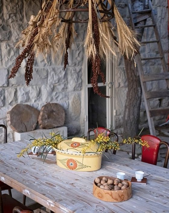 The outdoor table set with dried herb bundles and wildflowers hanging above it, wicker baskets and a bowl of walnuts on the wood
