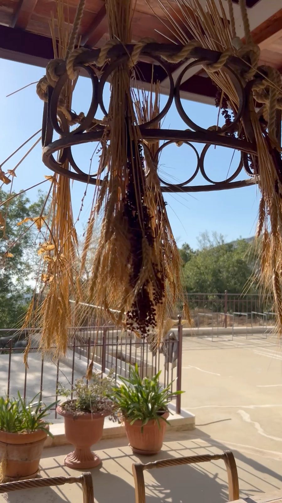 Bundles of wheat and dried herbs hanging to dry from a wrought-iron chandelier under the terrace roof, potted plants below